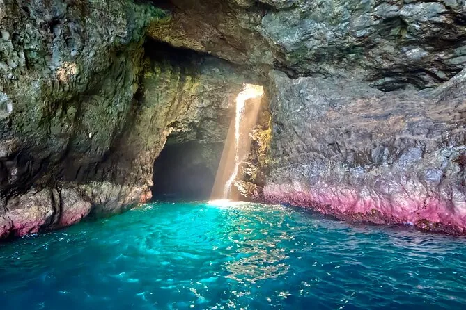 Sunlight falling into a sea cave onto turquoise water and pink rock