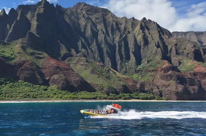 A yellow raft speeding along the foot of the green Na Pali cliffs