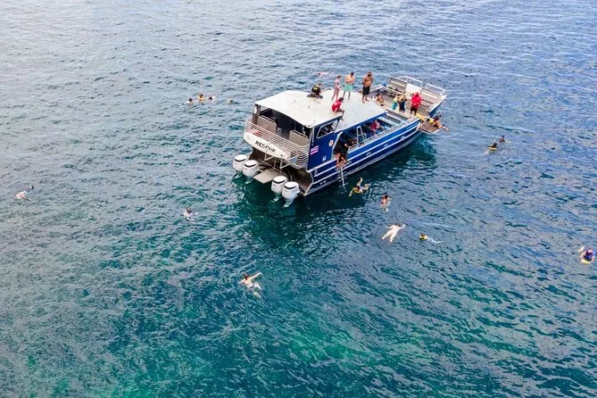Snorkelers in clear blue water beside a catamaran